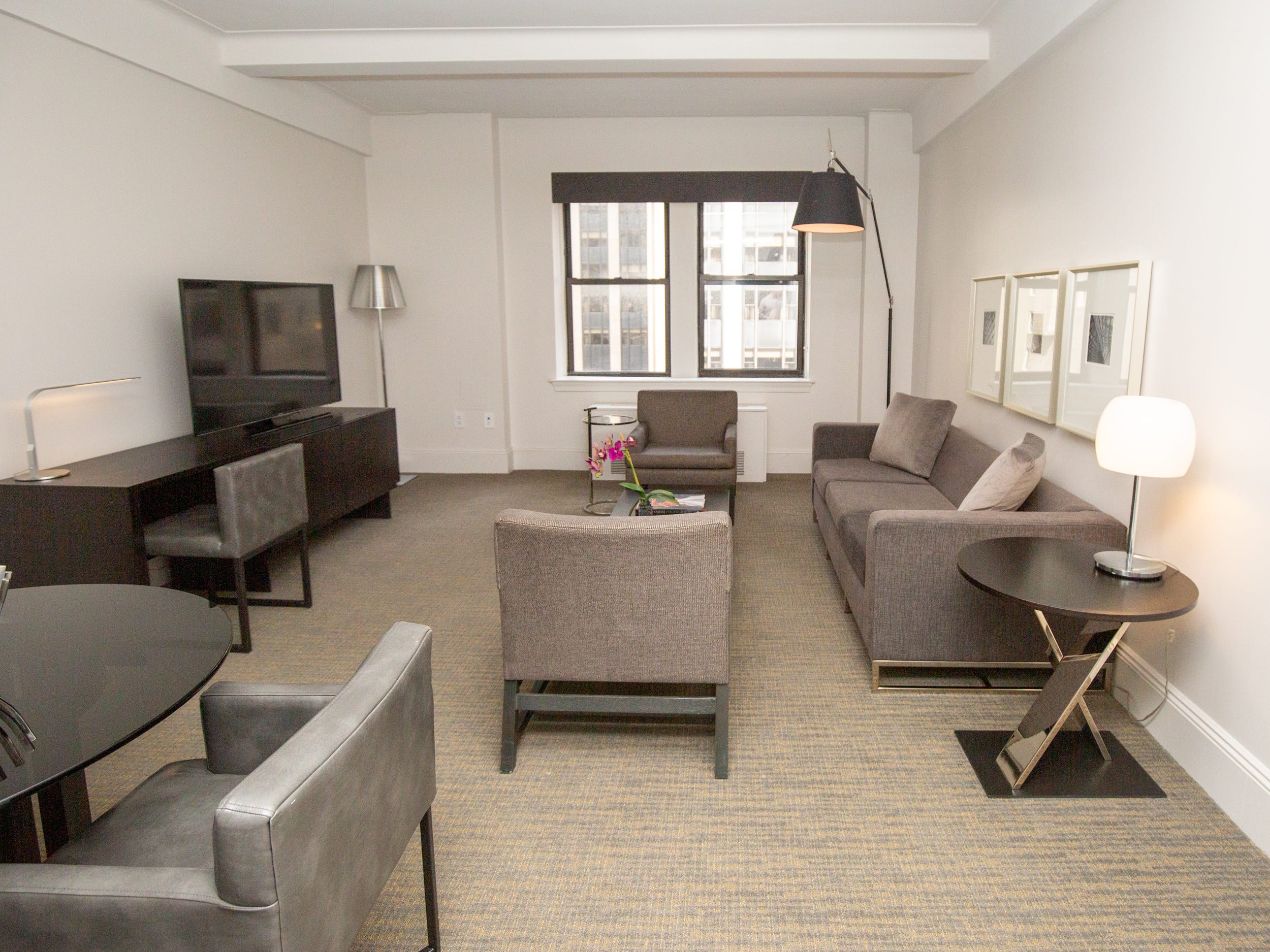 The living room with couches, seats, wall decor, a coffee table, and lights inside a suite at AKA Central Park.