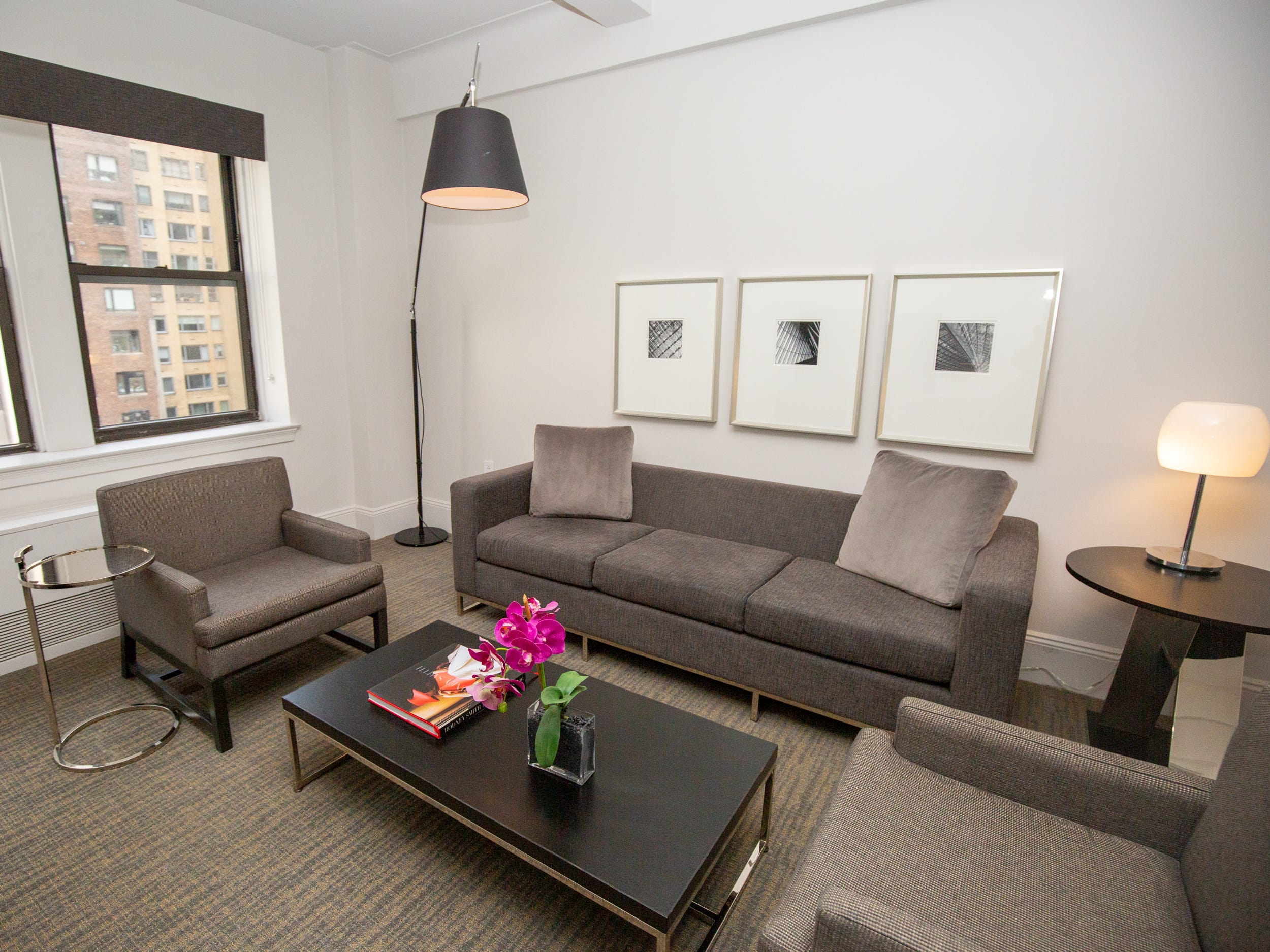 The living room with couches, seats, wall decor, a coffee table, and lights inside a suite at AKA Central Park.