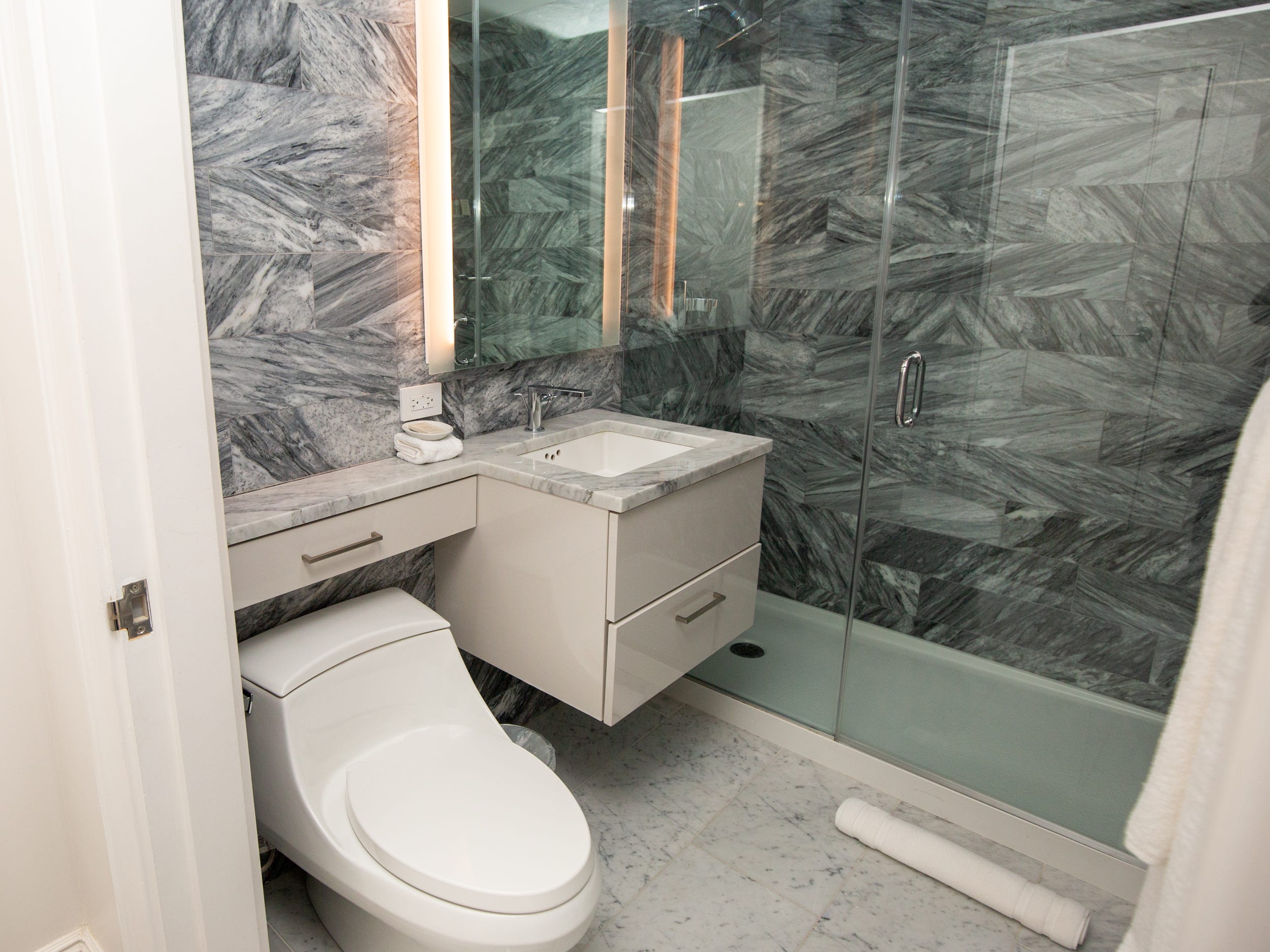 A marble bathroom with a sink, toilet, shower, vanity.
