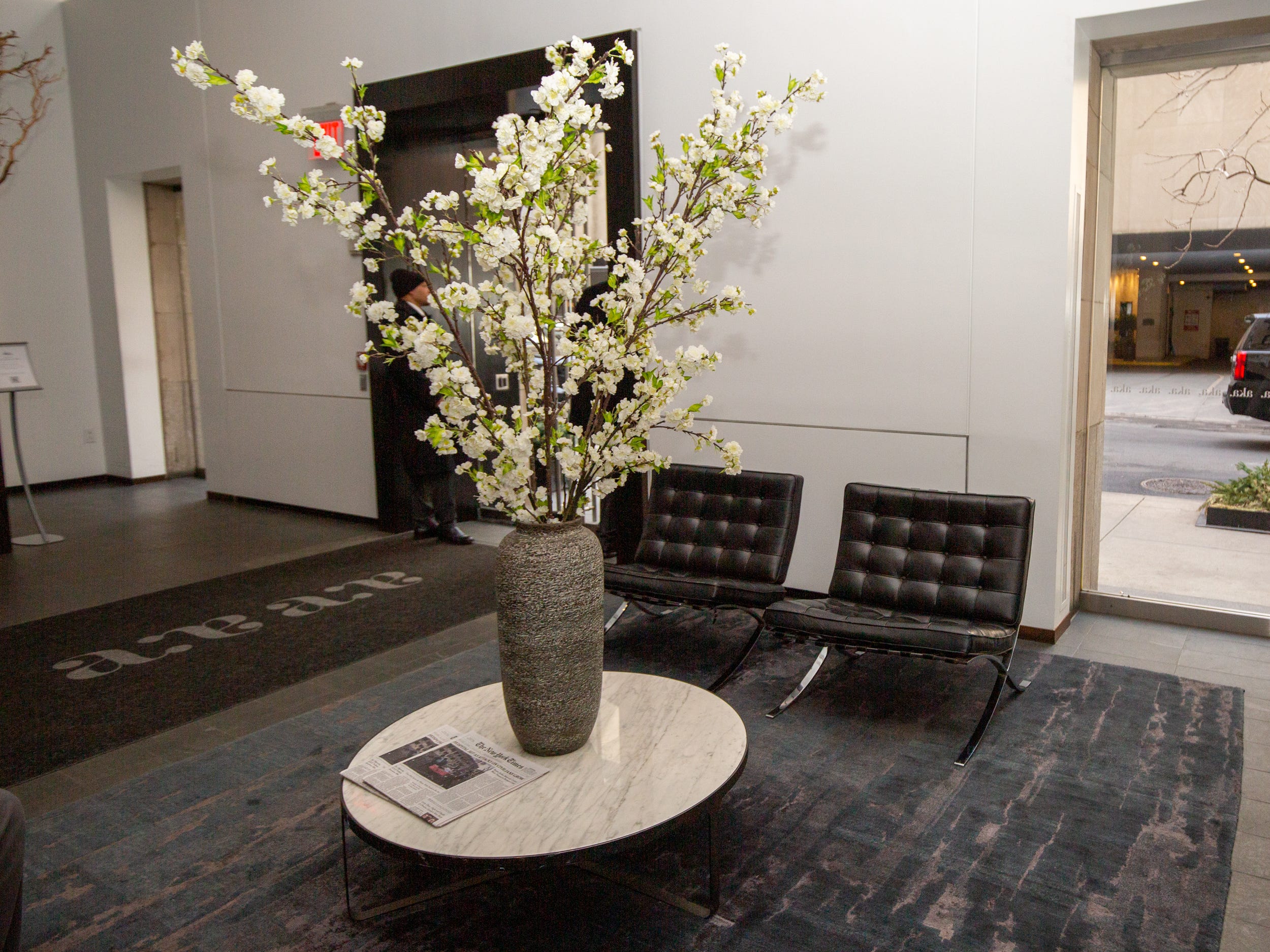 A vase with tall white plants on a table next to two lounge chairs.